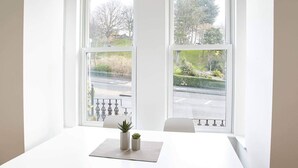 A room with a white table and two windows with a view of a street and greenery. - Host Stay Park View Apartment (Whitby)