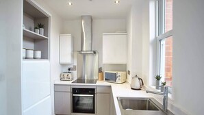 A modern kitchen with white cabinetry, a stainless steel range hood, a built-in oven, a microwave, and a sink. - Host Stay Park View Apartment (Whitby)