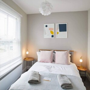 A hotel room with a bed, two bedside tables, a window with blinds, and two abstract wall art pieces. - Host Stay Windsor Cottage (Saltburn-by-the-Sea)