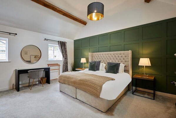 A bedroom with a bed, bedside tables, a desk, a chair, a lamp, a mirror, and a hanging light fixture.