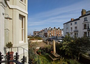 A residential street with a row of terraced houses, a clear sky, and a small garden area with a wooden bench.
