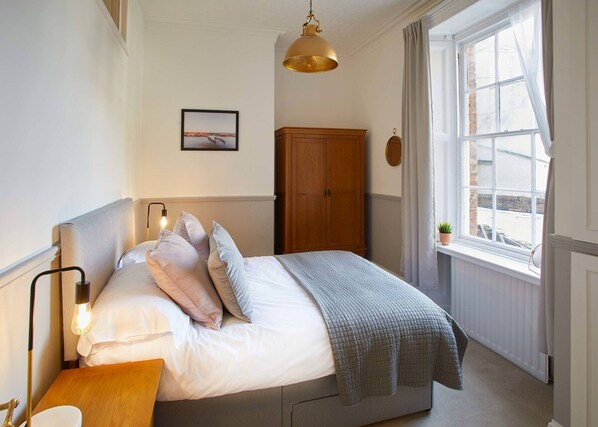 A bedroom with a bed, bedside lamp, wooden wardrobe, and a window with curtains.