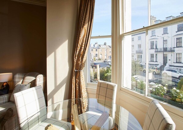 A room with a glass table and chairs, a view of the city through large windows, and a plaid-patterned sofa. - Host Stay Havelock Place Apartment (Whitby)