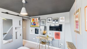 Une chambre moderne avec un lit, un bureau et une chaise. Plusieurs tableaux encadrés ornent le mur.
