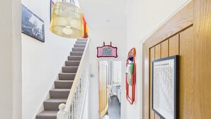 Un escalier menant à une pièce où l’on trouve un texte encadré au mur, une porte avec une pancarte et une lampe suspendue.