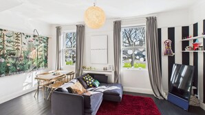 Un salon moderne avec un canapé gris, un tapis rouge et une grande fenêtre agrémentée de rideaux.