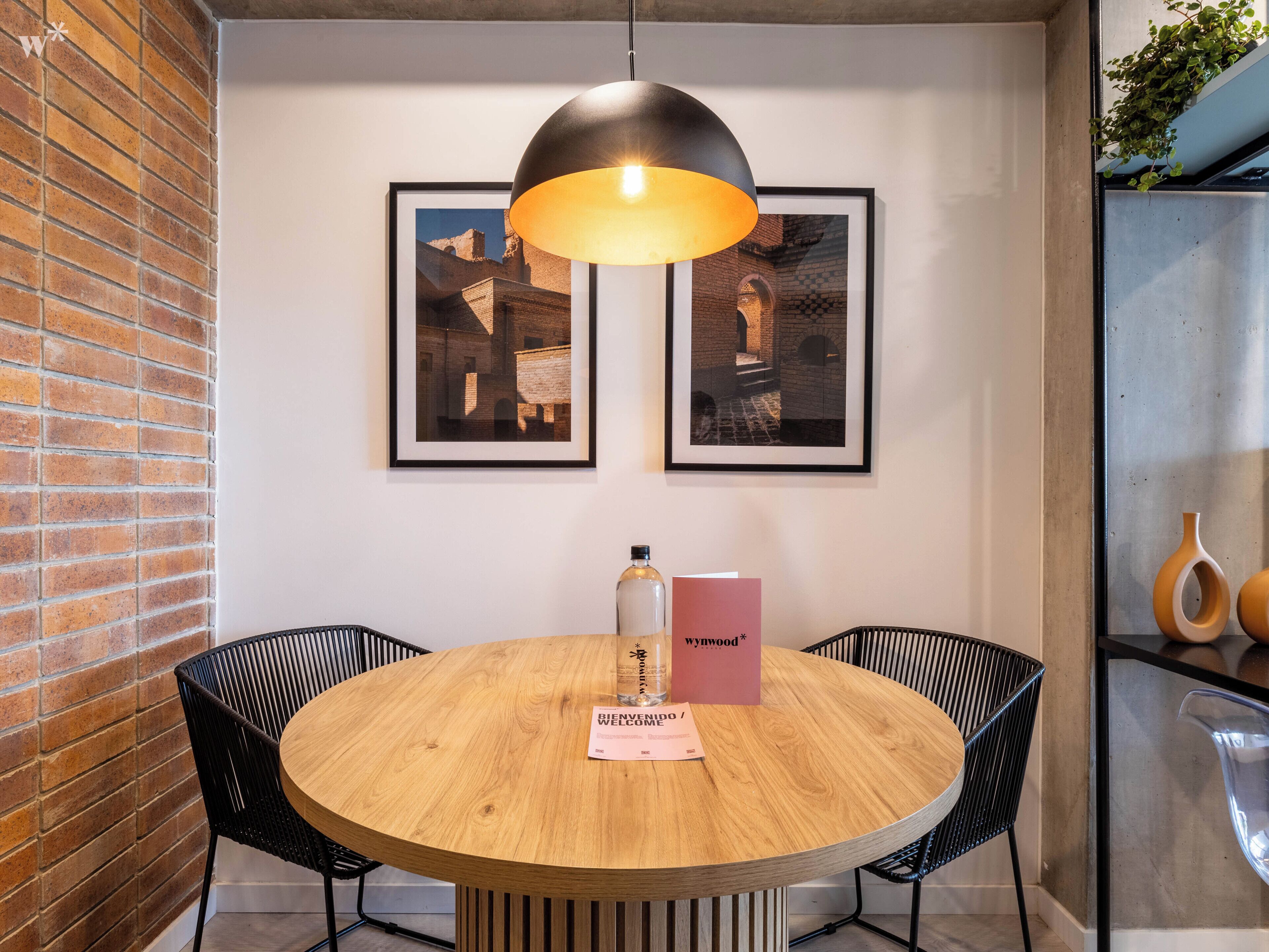 Una mesa redonda de madera con dos sillas, una lámpara colgante y dos cuadros en la pared.