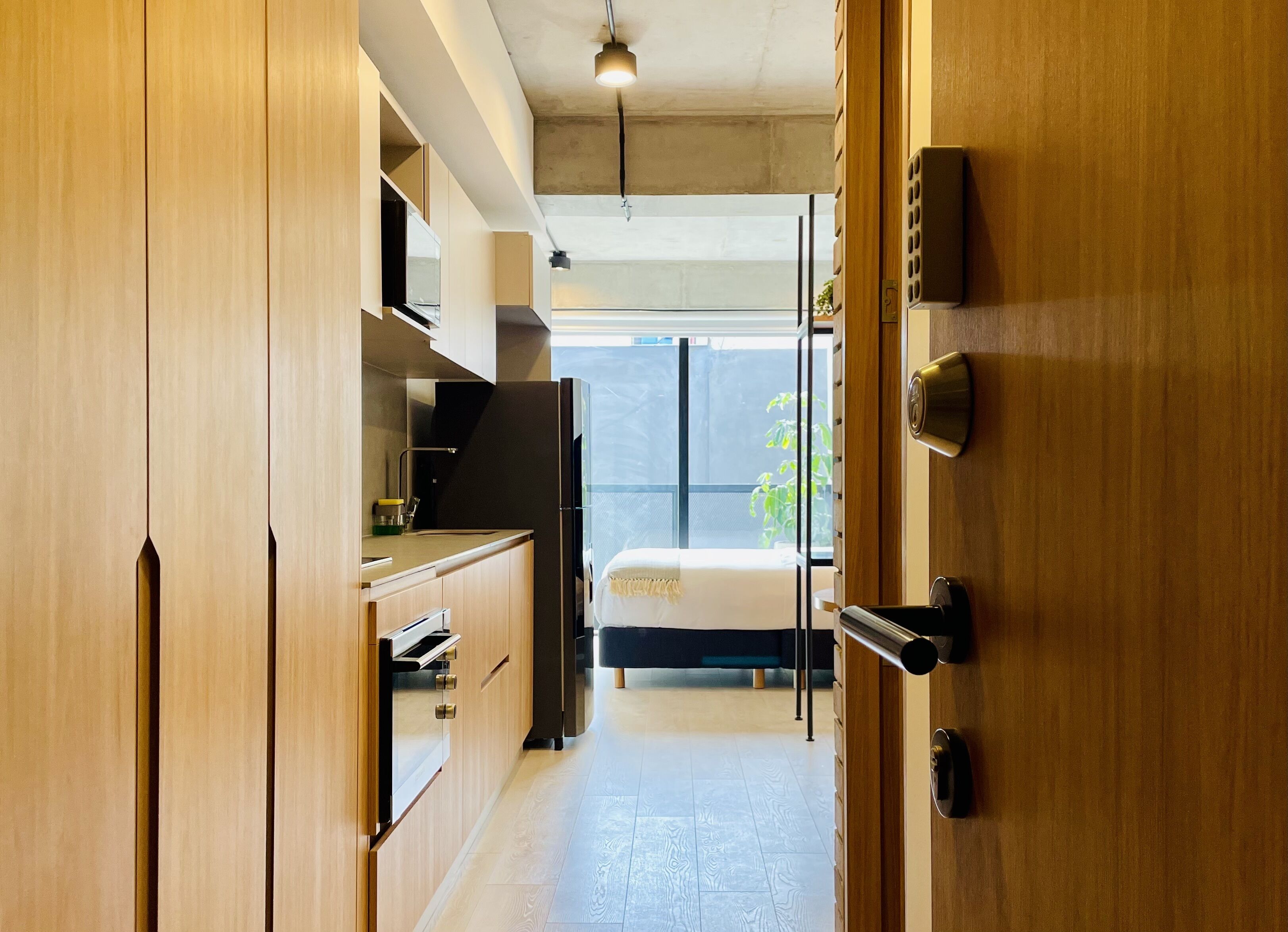 A compact kitchen with wooden cabinets, a built-in oven, and a window overlooking a balcony.