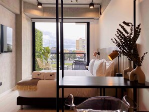 Ein modernes Hotelzimmer mit großem Fenster, einer Couch, einem Esstisch und einer Zimmerpflanze.