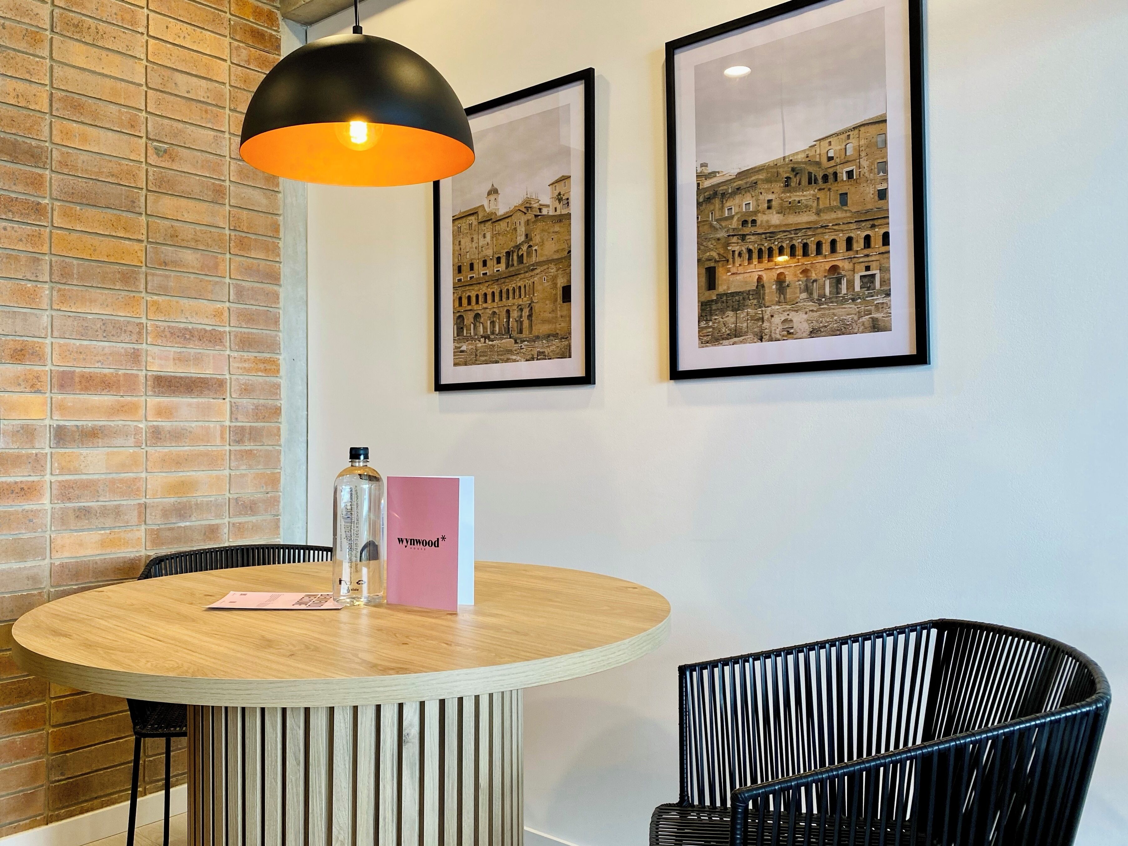 A round wooden table with a black chair, a bottle, and a pink card on it.