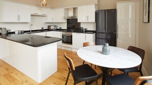 Een moderne keuken met witte kasten, een zwart aanrecht, een marmeren eiland en een ronde eettafel met stoelen.