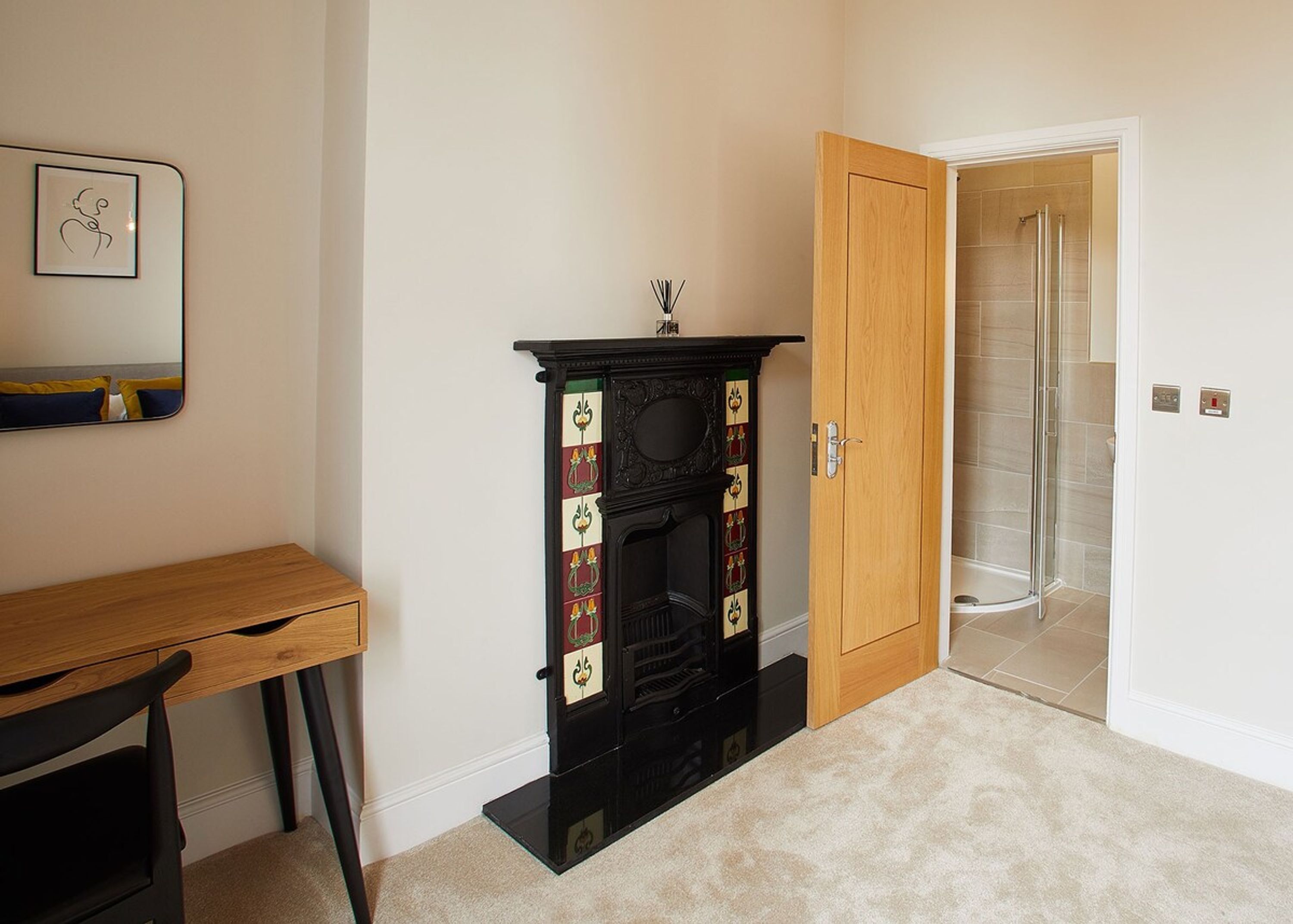 Una habitación con un escritorio de madera, una chimenea negra con paneles decorativos y una puerta de ducha de vidrio.