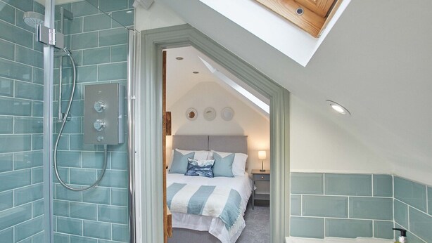 A modern bathroom with a glass shower enclosure, a visible control panel, and a skylight above the bedroom. - Host Stay Threadneedle Cottage (Whitby)