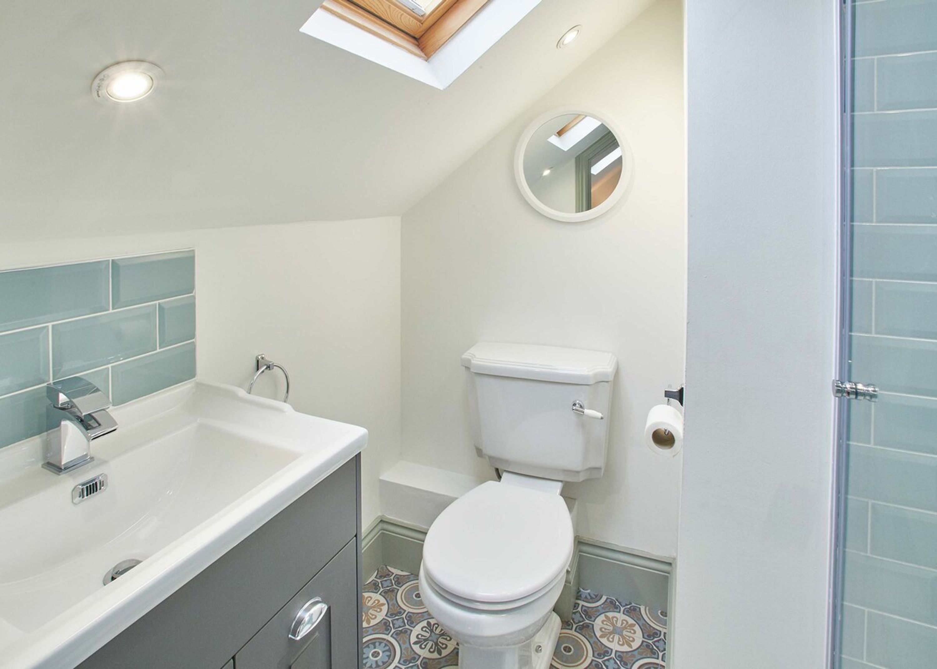 A bathroom with a skylight, a toilet, and a sink with a mirror.