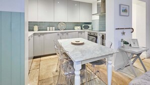 A modern kitchen with white cabinets, a marble countertop, and a dining area with clear chairs. - Host Stay The Courtyard Retreat (Whitby)