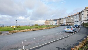 A street with terraced houses, a grassy area, and a road with cars. - Host Stay The Courtyard Retreat (Whitby)