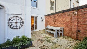 A courtyard with a white wall, a brick wall, a metal clock, and a table with chairs. - Host Stay The Courtyard Retreat (Whitby)