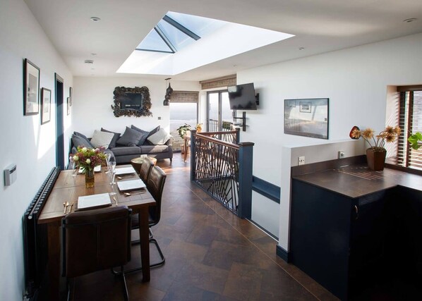 A modern kitchen with a dining area, a sofa, and a TV mounted on the wall. - Host Stay The Nook (Saltburn-by-the-Sea)