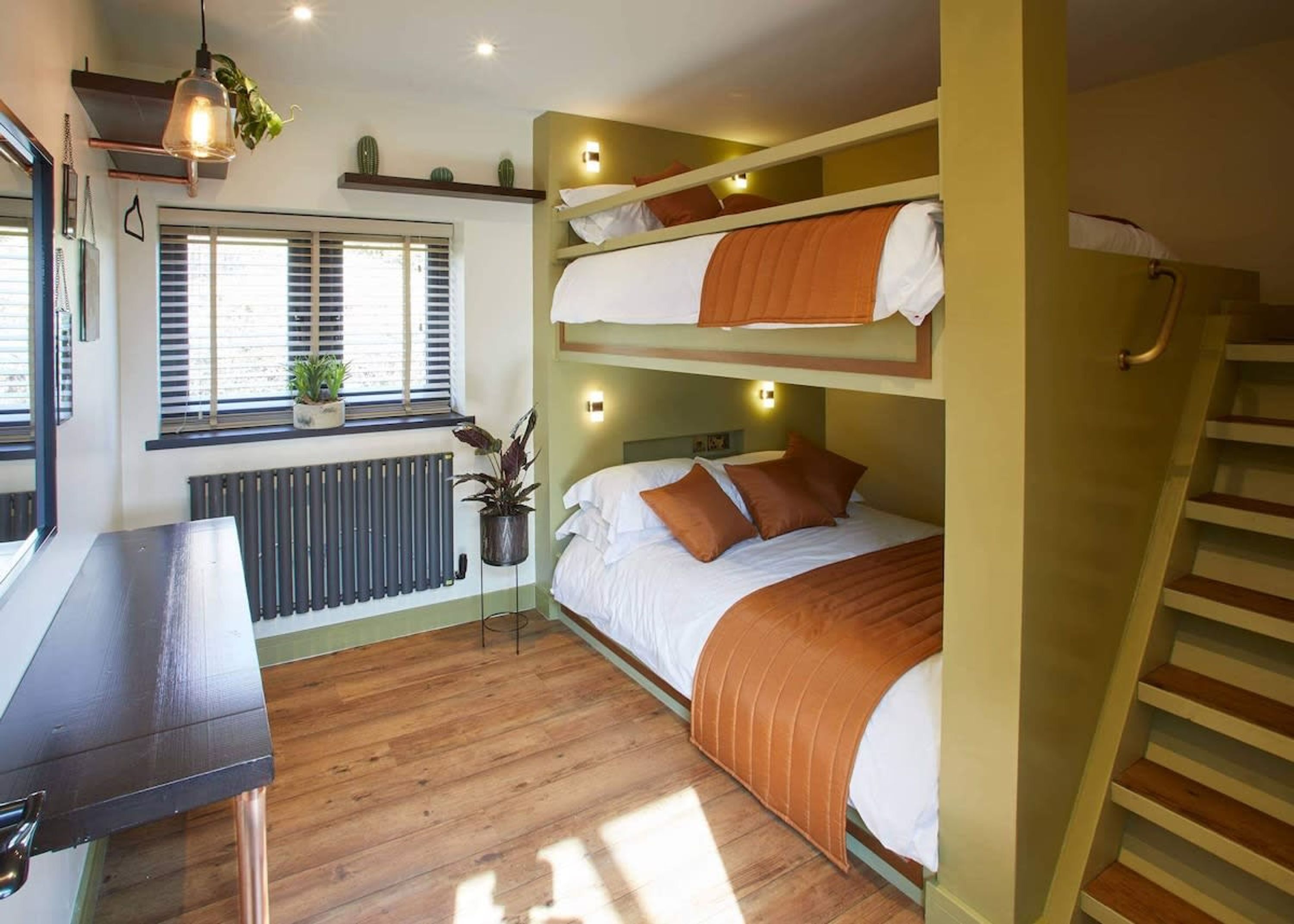 Ein Schlafsaalzimmer mit einem Schreibtisch, Topfpflanzen und einer Treppe.