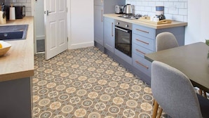 Uma cozinha compacta com armários cinza, painel de azulejos e piso estampado.