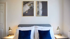 Quarto com uma cama, duas mesas de cabeceira e duas pinturas penduradas na parede.