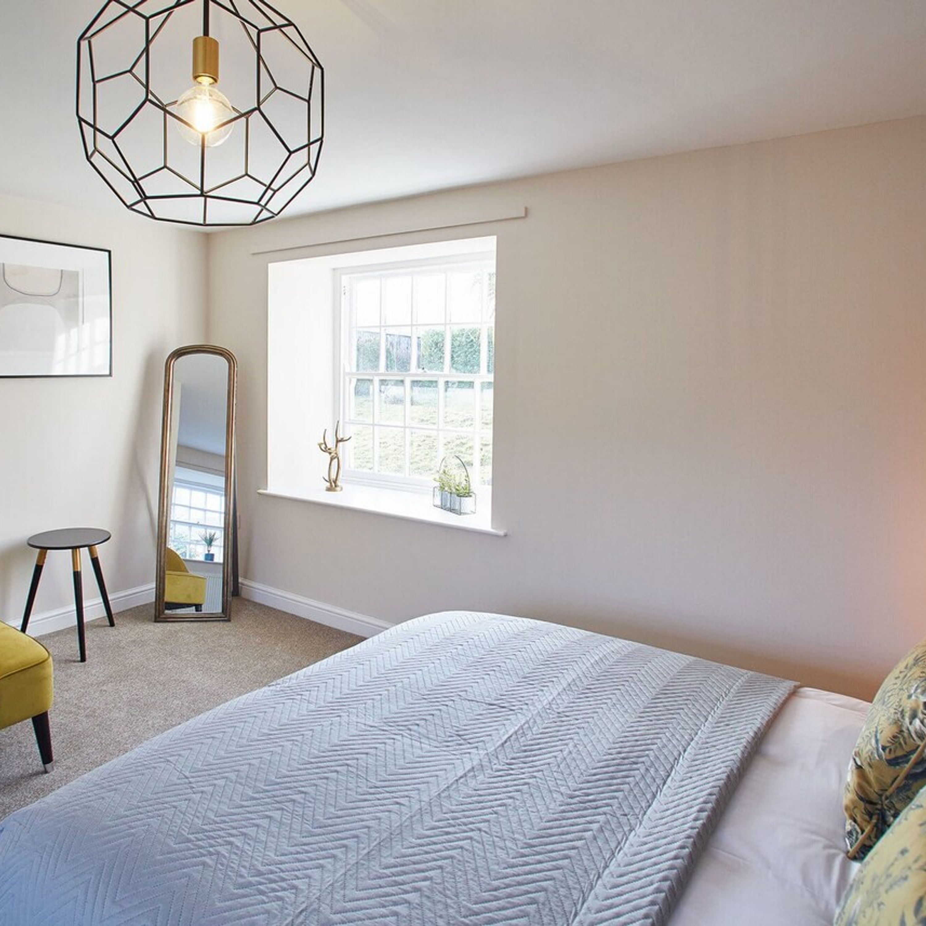 A bedroom with a large bed, a window with a view, a mirror, and a geometric light fixture.