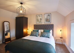 Une chambre à coucher avec un grand lit, une armoire sombre, un miroir et deux œuvres d’art encadrées accrochées au mur.