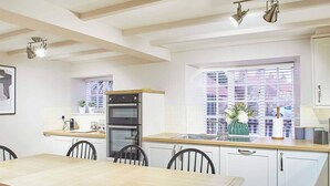 A modern kitchen with white cabinets, a wooden dining table, and a built-in oven. - Host Stay Middle Farmhouse (Whitby)