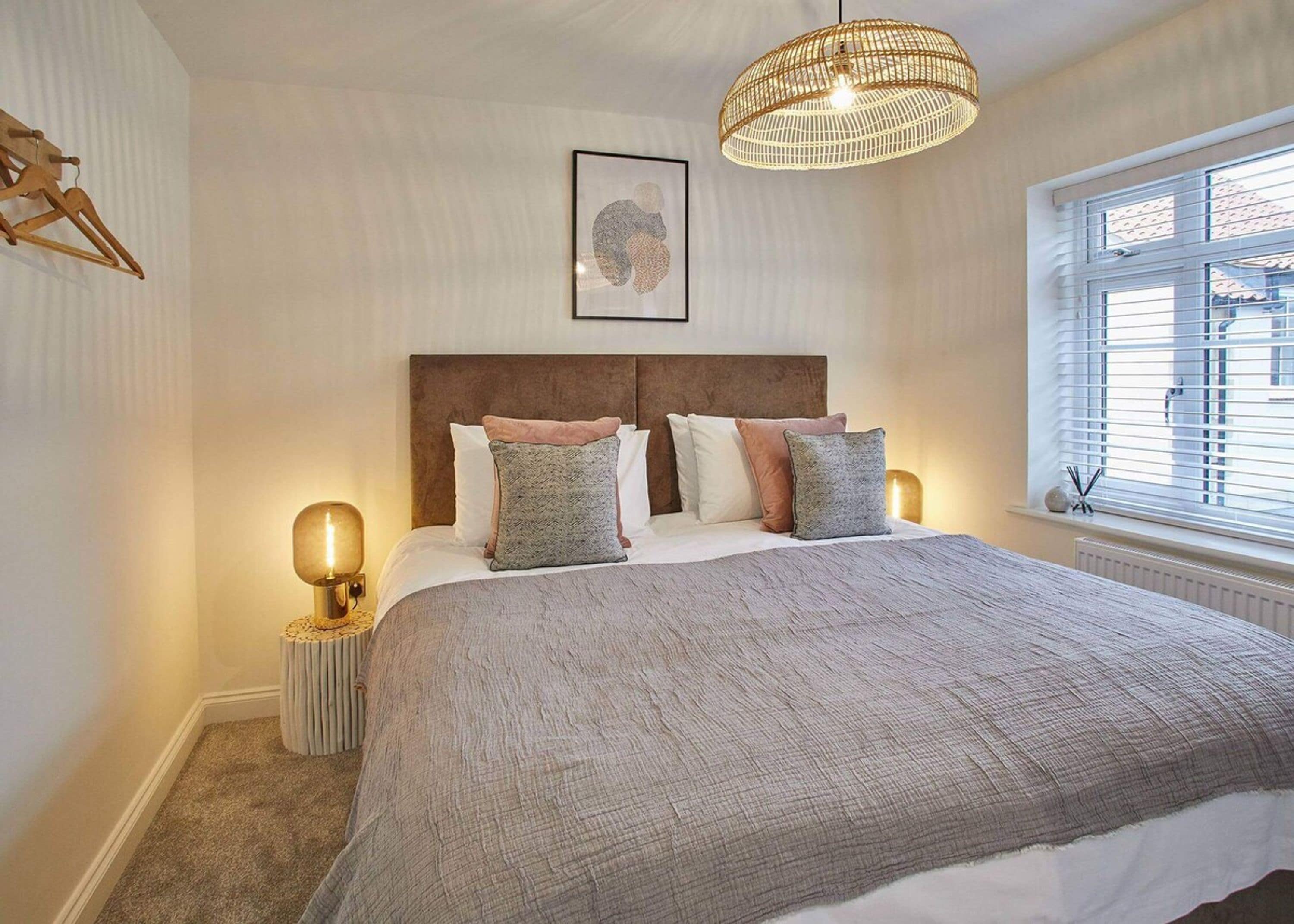Une chambre à coucher avec un grand lit, une tête de lit en bois, un luminaire suspendu et une fenêtre avec des stores.