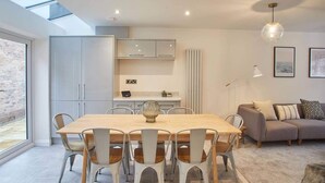 Una cocina moderna con armarios blancos, una mesa de comedor con sillas y un sofá en un área de estar con vista al mar.