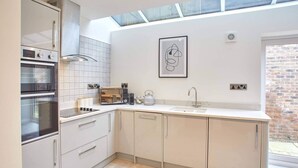 A modern kitchen with a built-in oven, microwave, and kettle, a large window, and a framed abstract artwork on the wall.
