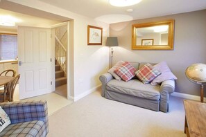 Cozy living space with a sofa, armchair, and dining area, featuring a staircase to an upper level.