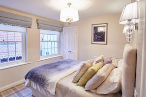 Cozy retreat with a large bed, chandelier, and framed artwork, featuring two windows and a door.