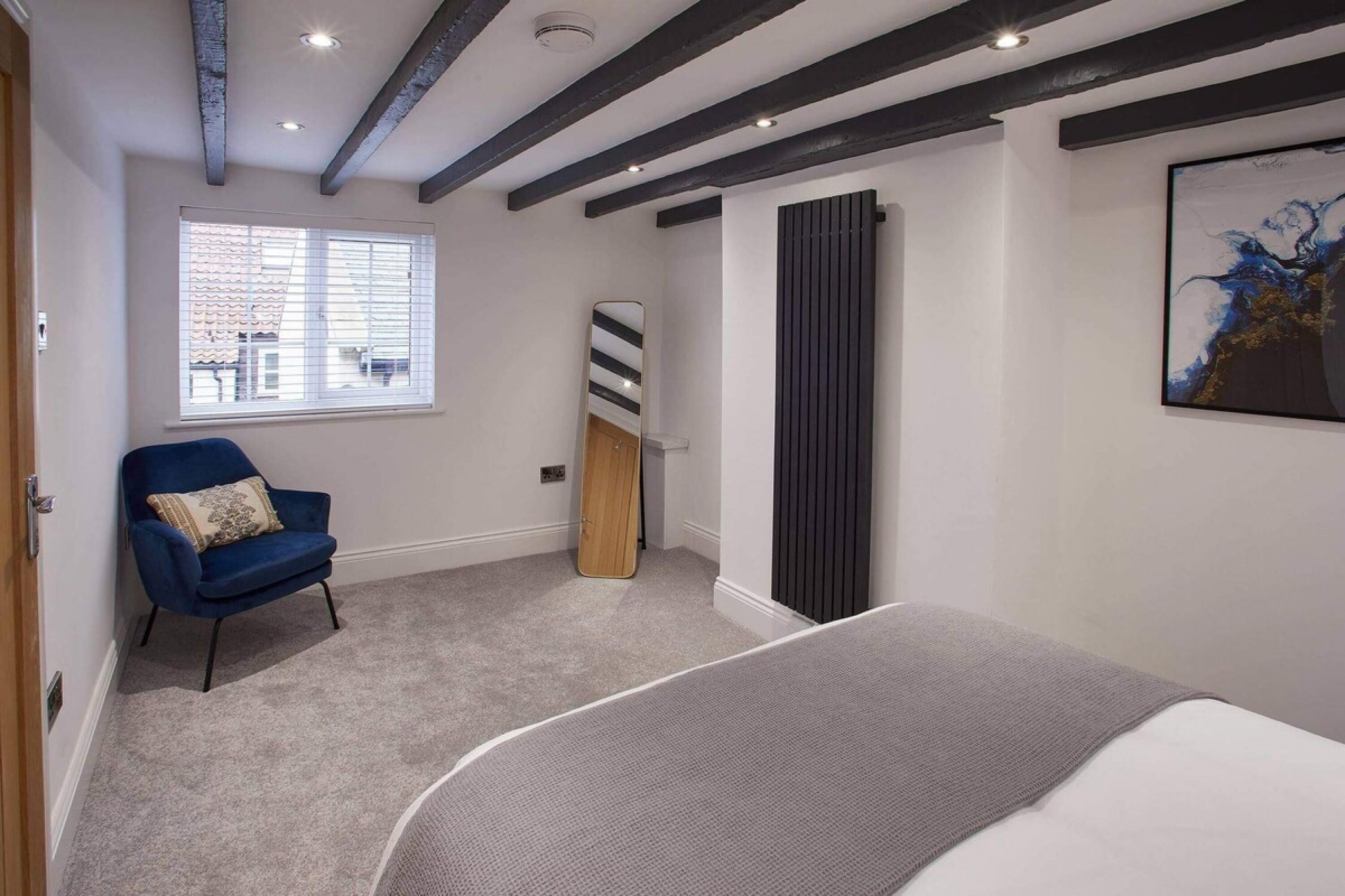 A bedroom with a bed, a chair, a window, and a painting on the wall.