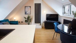 En modern lägenhet i loftstil med ett takfönster, en matplats, ett vardagsrum med TV och ett stort fönster med utsikt över staden.