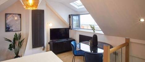 A modern loft apartment with a dining area, a TV, and a skylight.