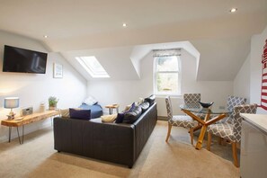 A modern loft-style living room with a dark leather sofa, a glass coffee table, patterned chairs, a flat-screen TV, and skylights. - Host Stay Number 3 at Pannett Apartments (Whitby)