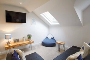 A modern living room with a flat-screen TV, a wooden table with a lamp, a bean bag, and a sofa. - Host Stay Number 3 at Pannett Apartments (Whitby)