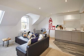 A modern apartment with a loft-style living area, a kitchen with white cabinetry, and a red lighthouse wall decal. - Host Stay Number 3 at Pannett Apartments (Whitby)