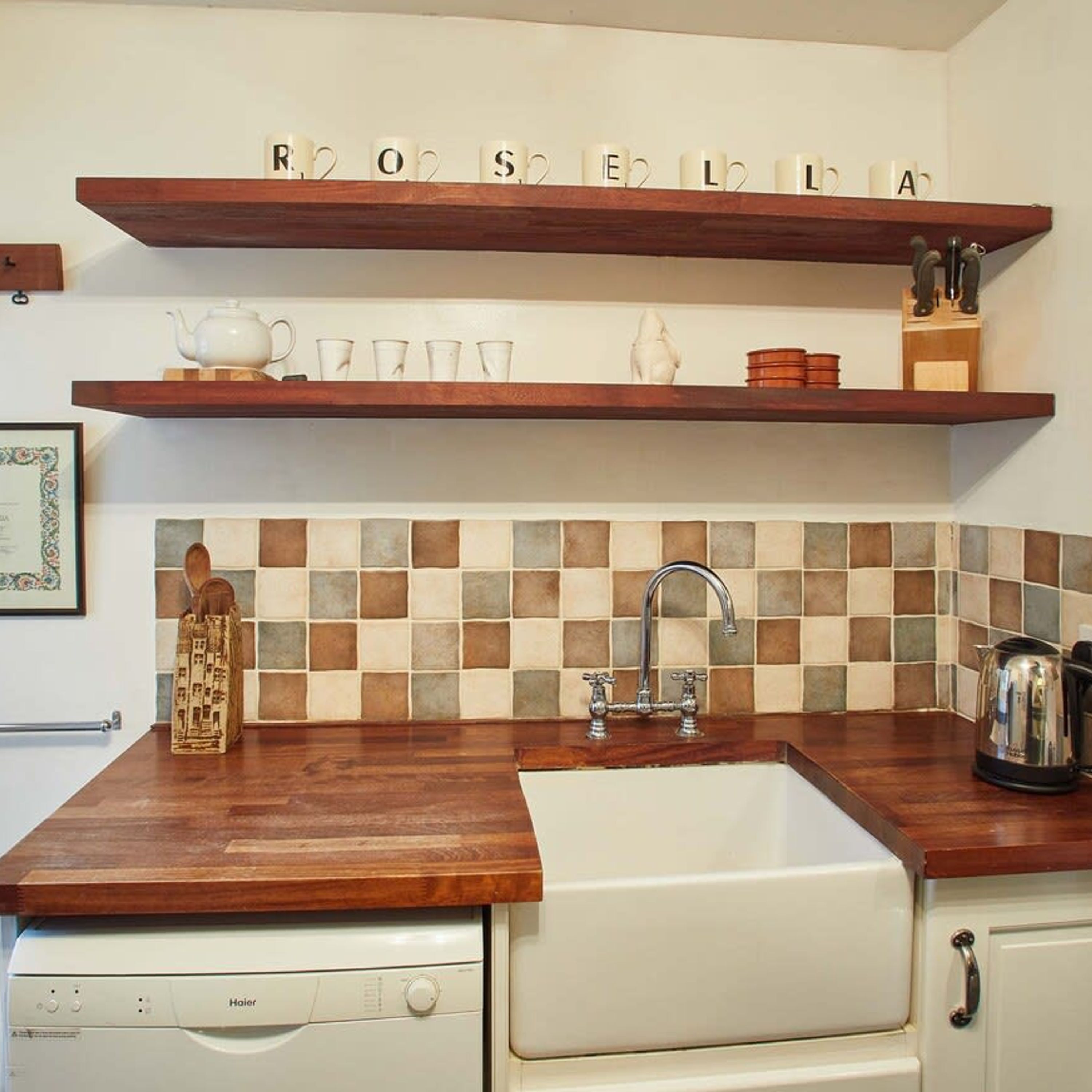 Una cocina con encimeras de madera, un fregadero y dos estantes de madera con tazas y utensilios de cocina.