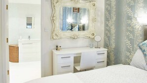 Quarto com uma cama grande, penteadeira branca, espelho e porta para um banheiro.