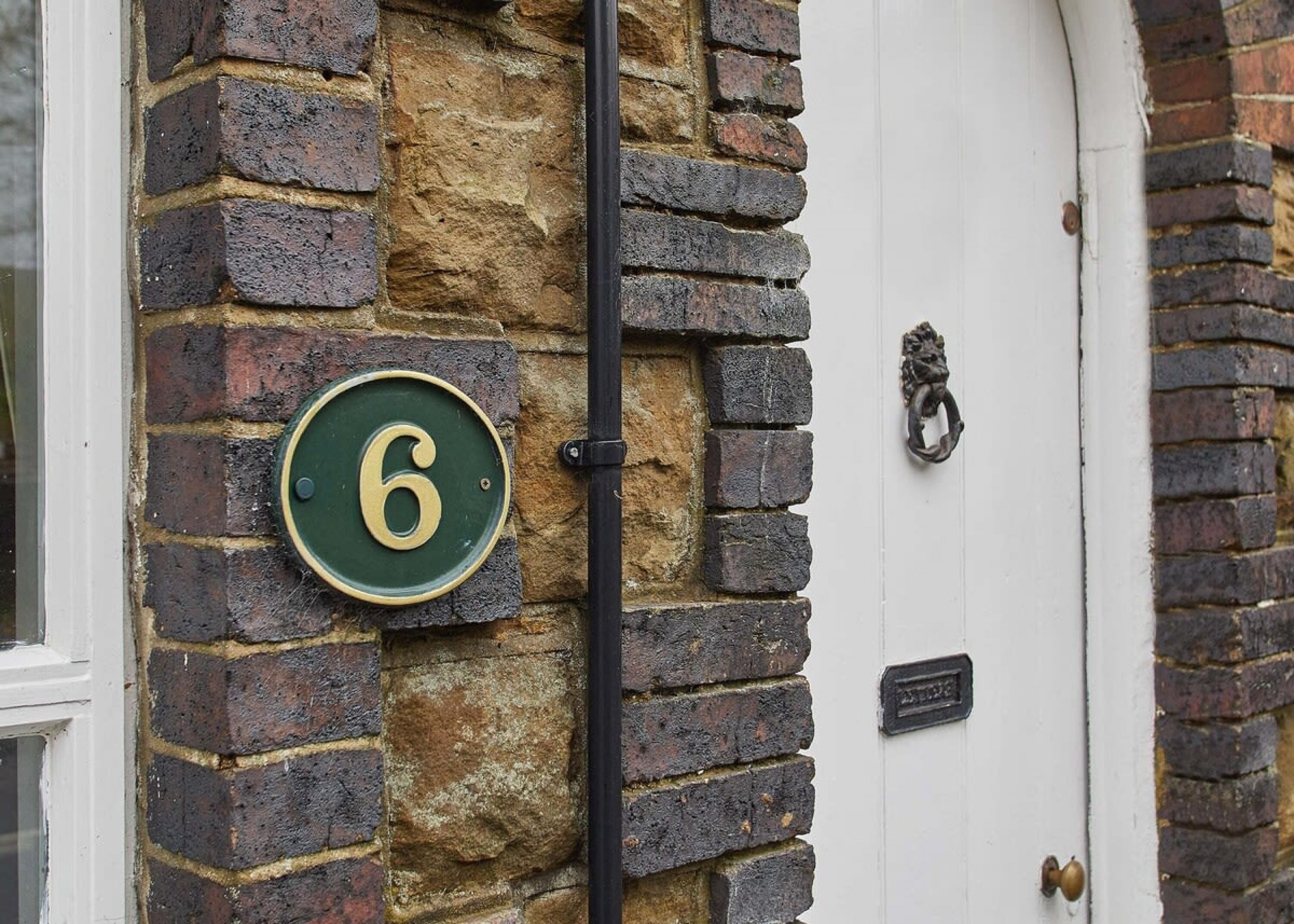 A brick wall with a green house number sign '6' and a white door with a knocker.