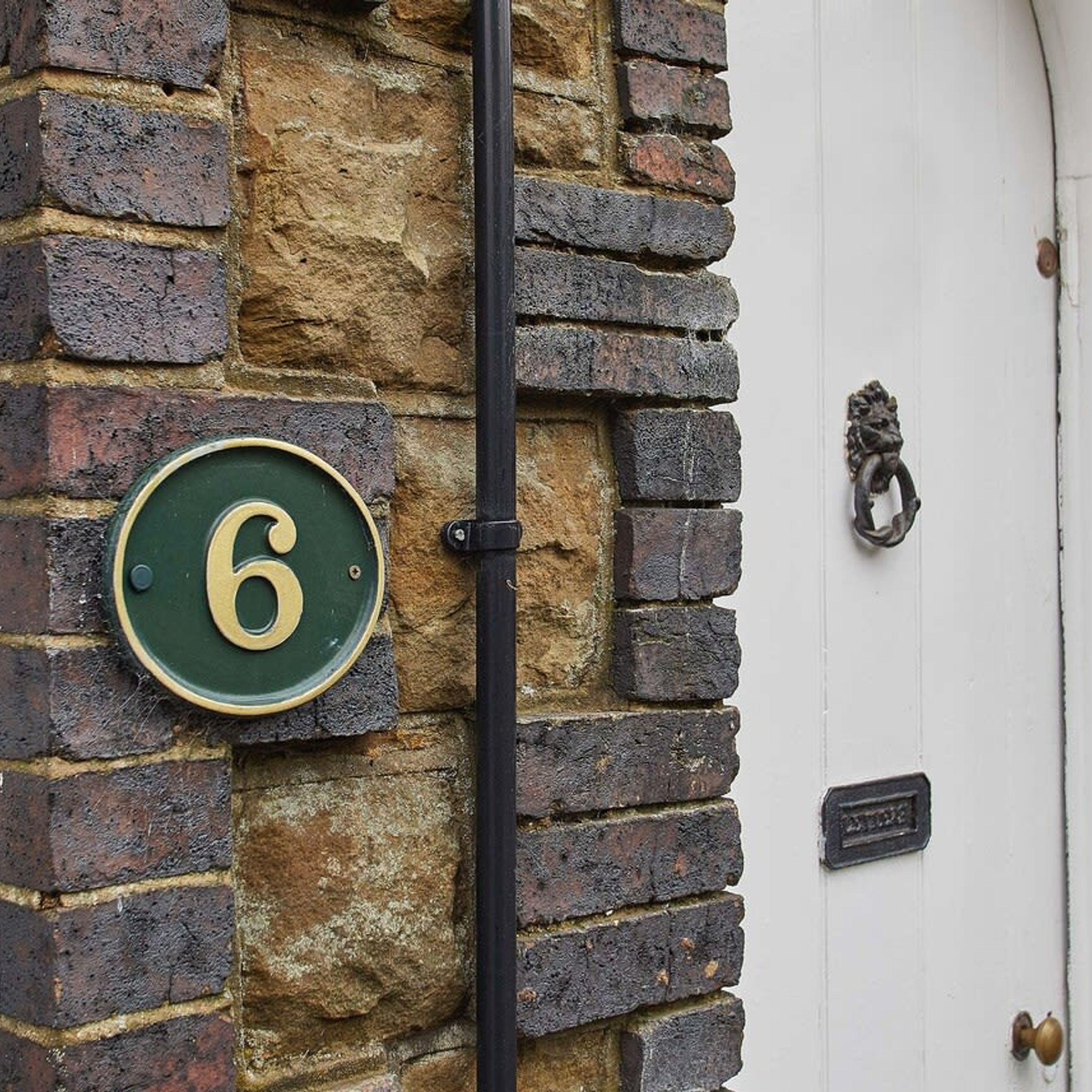 A house number 6 on a brick wall, a black metal pole, and a white door with a knocker.