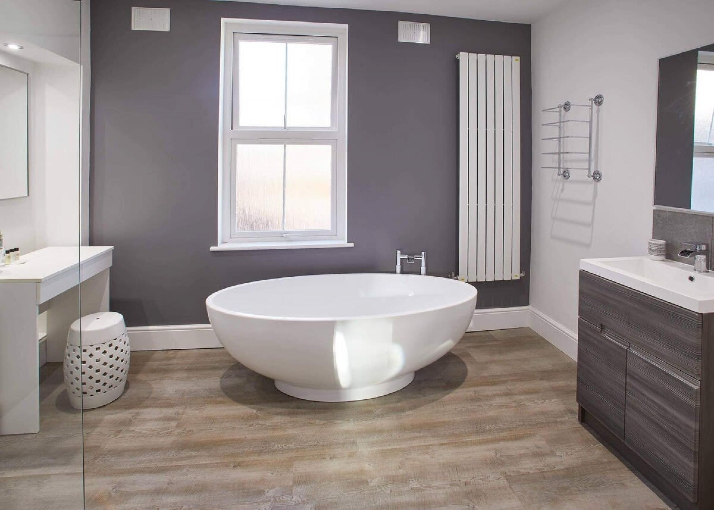 Une salle de bain moderne avec une baignoire sur pieds, une grande fenêtre, un radiateur et un meuble-lavabo avec un miroir.