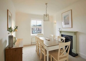 Enjoy meals in this cozy dining room with a fireplace, wooden table, and window offering a view of the surrounding buildings.