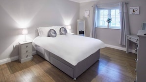 Un dormitorio con una cama grande, mesitas de noche, un espejo, un escritorio y una ventana con cortinas.