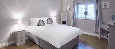 A bedroom with a large bed, bedside tables, a mirror, a desk, and a window with curtains.