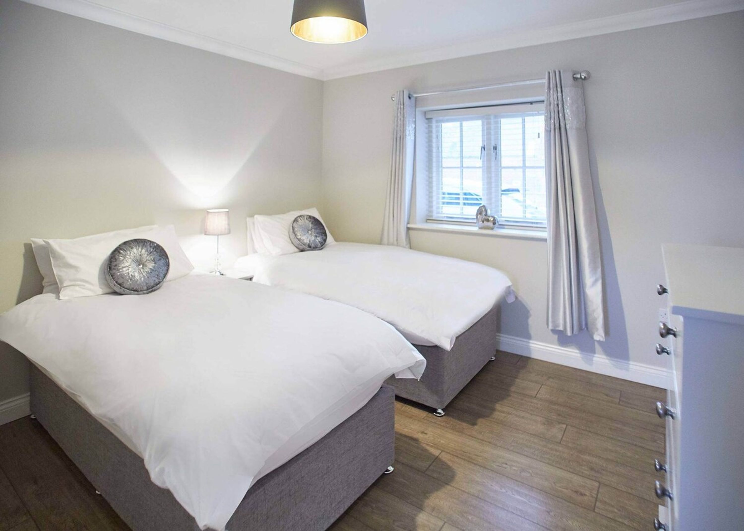 Une chambre avec deux lits, une fenêtre avec des rideaux, une lampe et une armoire.