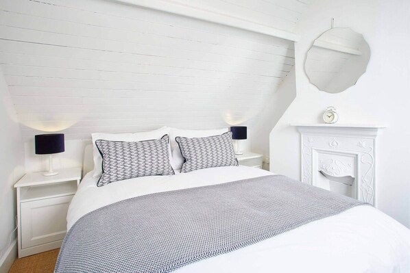 A white bedroom with a bed, two bedside tables with lamps, a mirror, and a fireplace. - Host Stay Gun Gutter House (Saltburn-by-the-Sea)