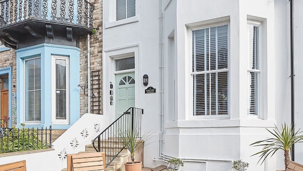 A courtyard with wooden furniture, potted plants, and a staircase leading to a building with a blue door and white walls.